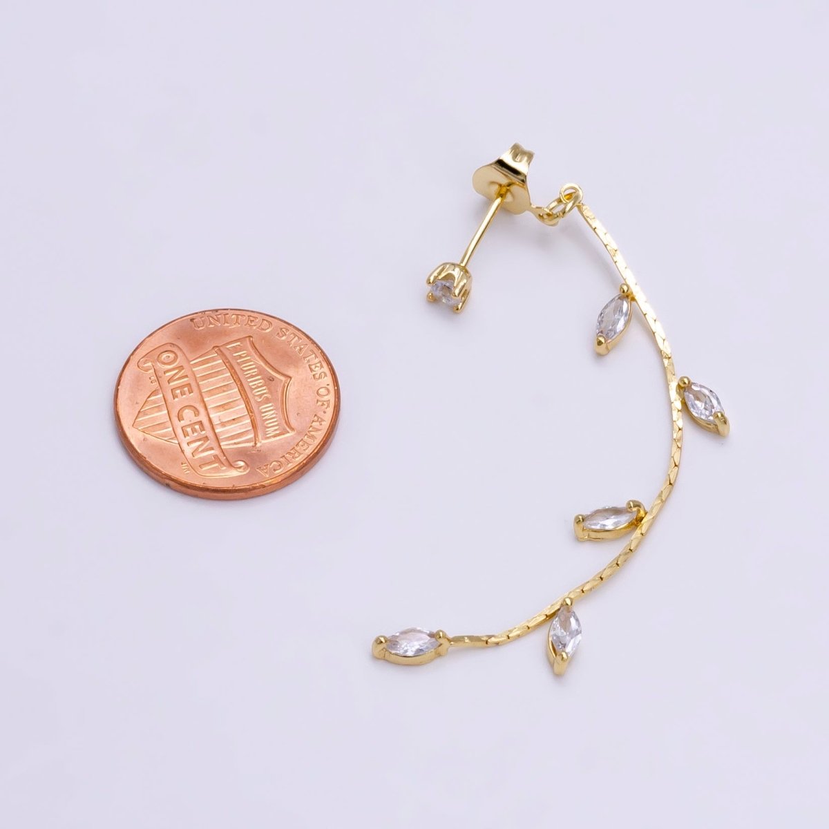 A gold-filled leaf drop stud earring with a delicate design featuring several cubic zirconia stones, displayed next to a penny for scale.