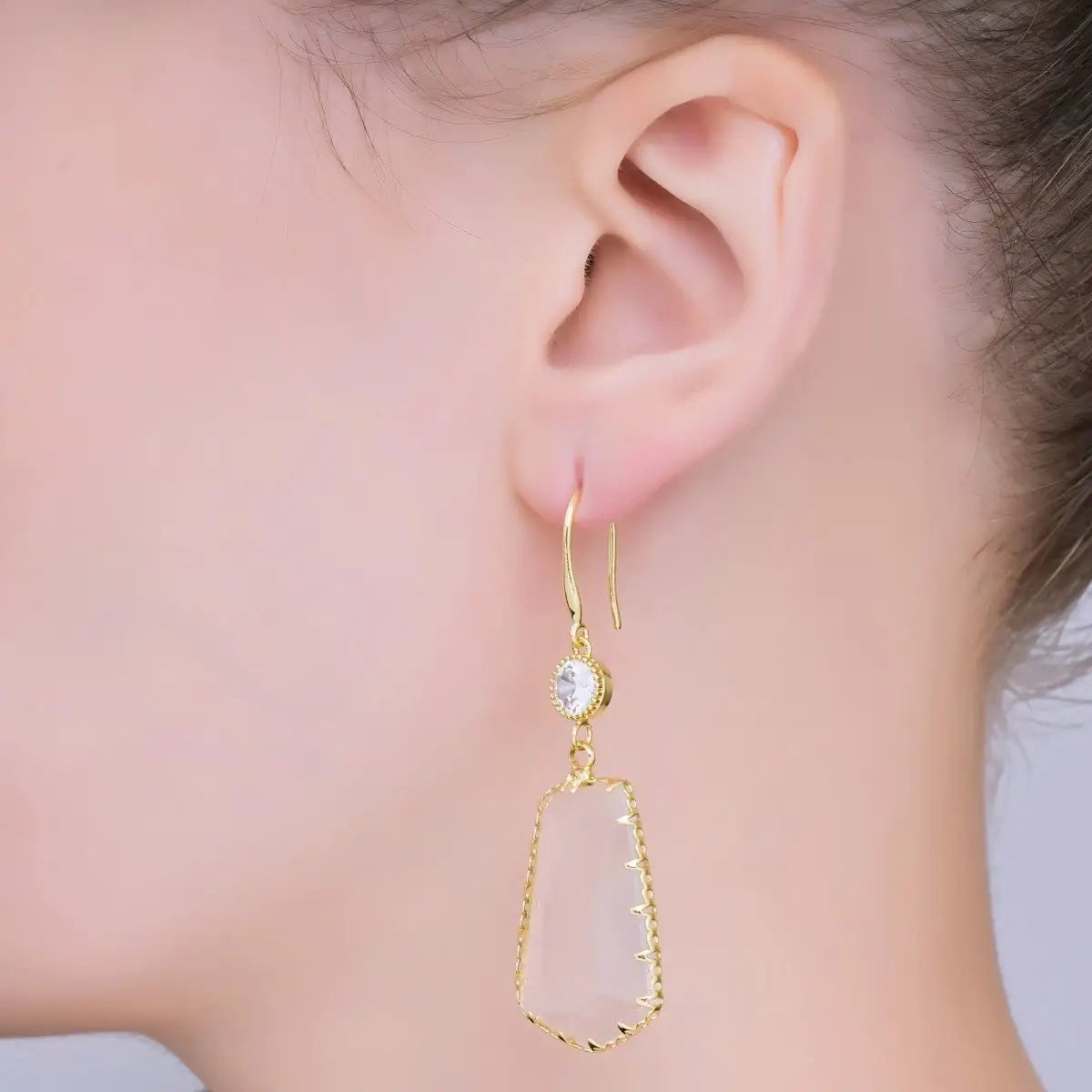 A close-up of a models ear showcasing elegant clear stone statement earrings. The earrings feature a gold-filled design with a cubic zirconia accent, perfect for adding a touch of glam to formal events like galas or weddings.