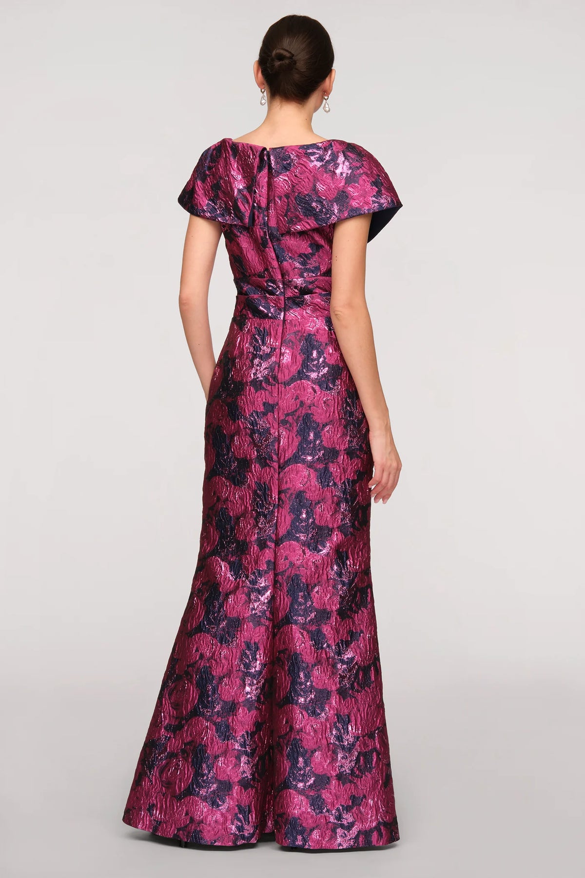 A woman stands in a stunning purple and pink floral jacquard mermaid gown, showcasing a draped collar and fitted silhouette. This elegant dress is perfect for a black-tie wedding or gala, conveniently located near Apex, Cary, and Raleigh.