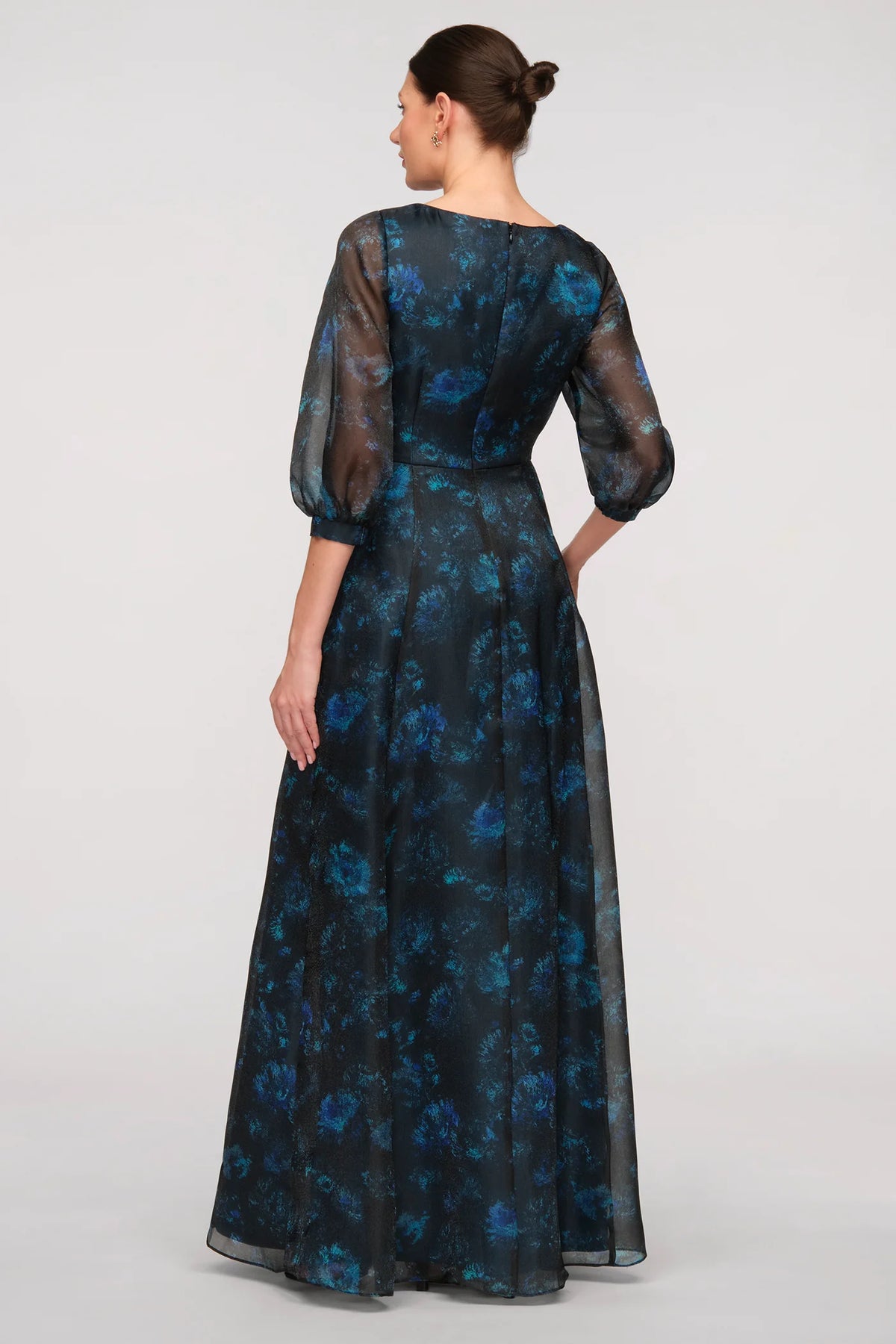 A model showcases a stunning floor-length gown featuring a floral print on sheer organza with a rich teal lining.