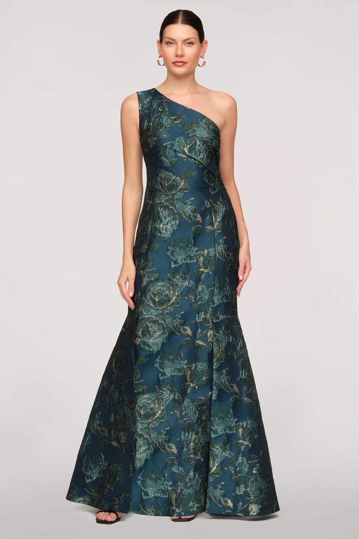 A model showcases a stunning teal one-shoulder gown featuring an elegant floral pattern, perfect for formal events such as weddings or galas.