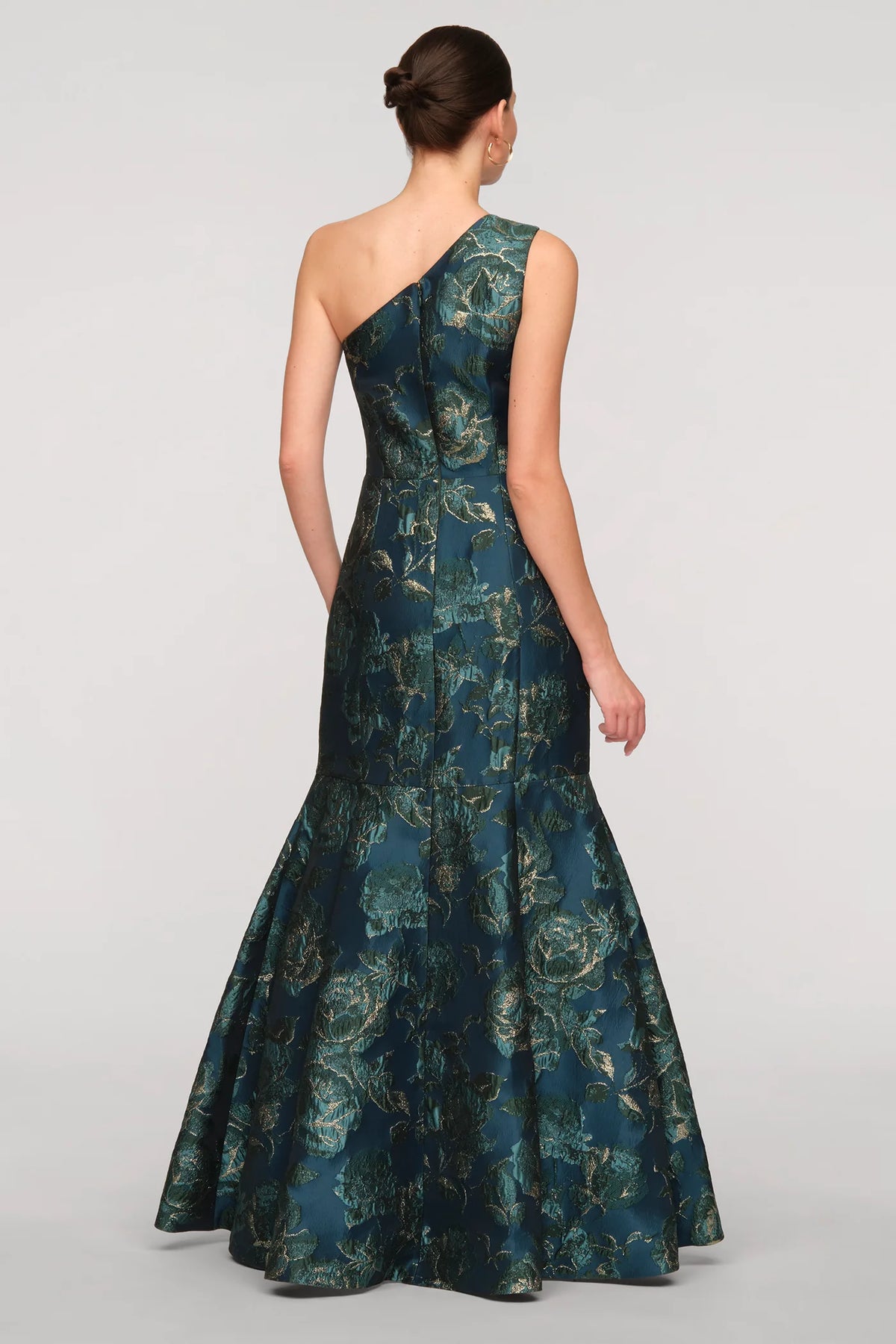 A model showcases a stunning teal gown with a one-shoulder design and a fitted silhouette, featuring a full skirt that flares elegantly.