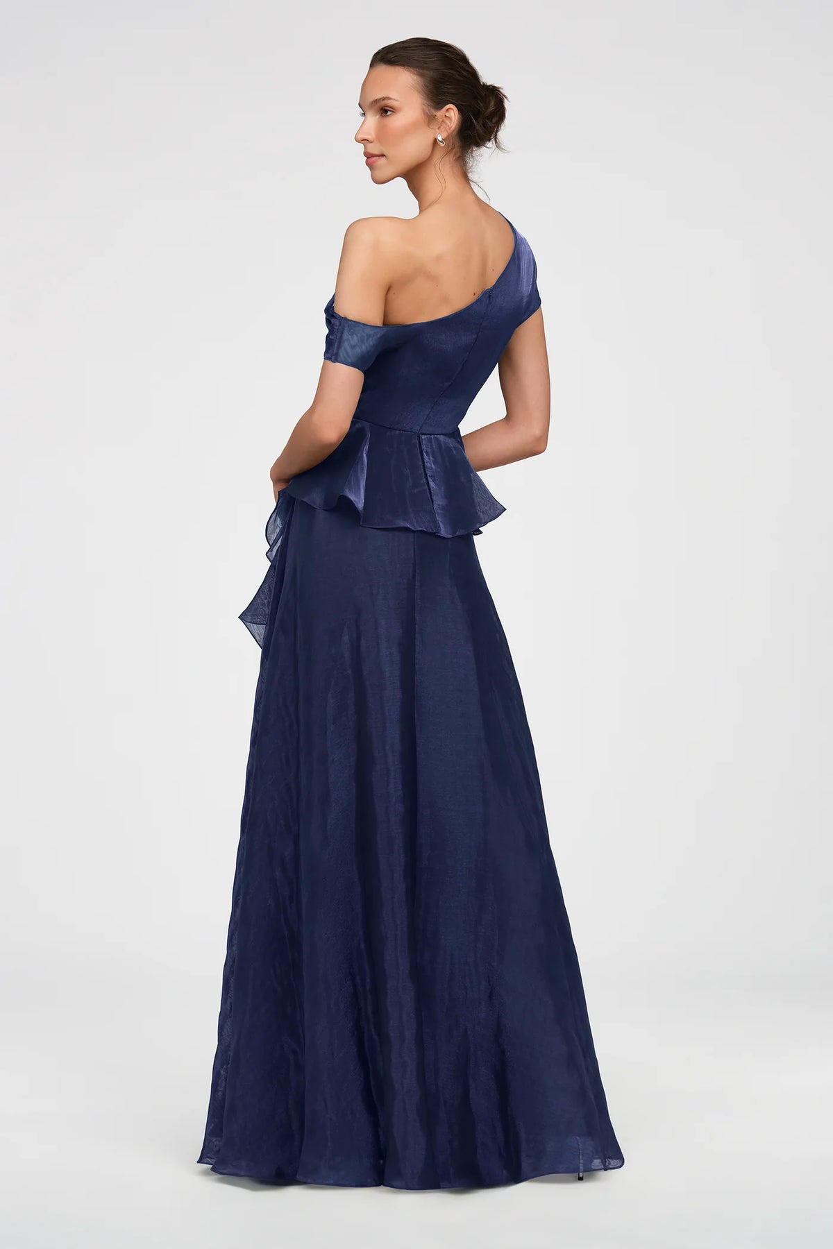A model showcases a stunning navy gown featuring an asymmetric neckline and a soft peplum overlay, perfect for elegant events like galas or black-tie weddings. This beautiful dress is conveniently located near Apex, Cary, and Raleigh.