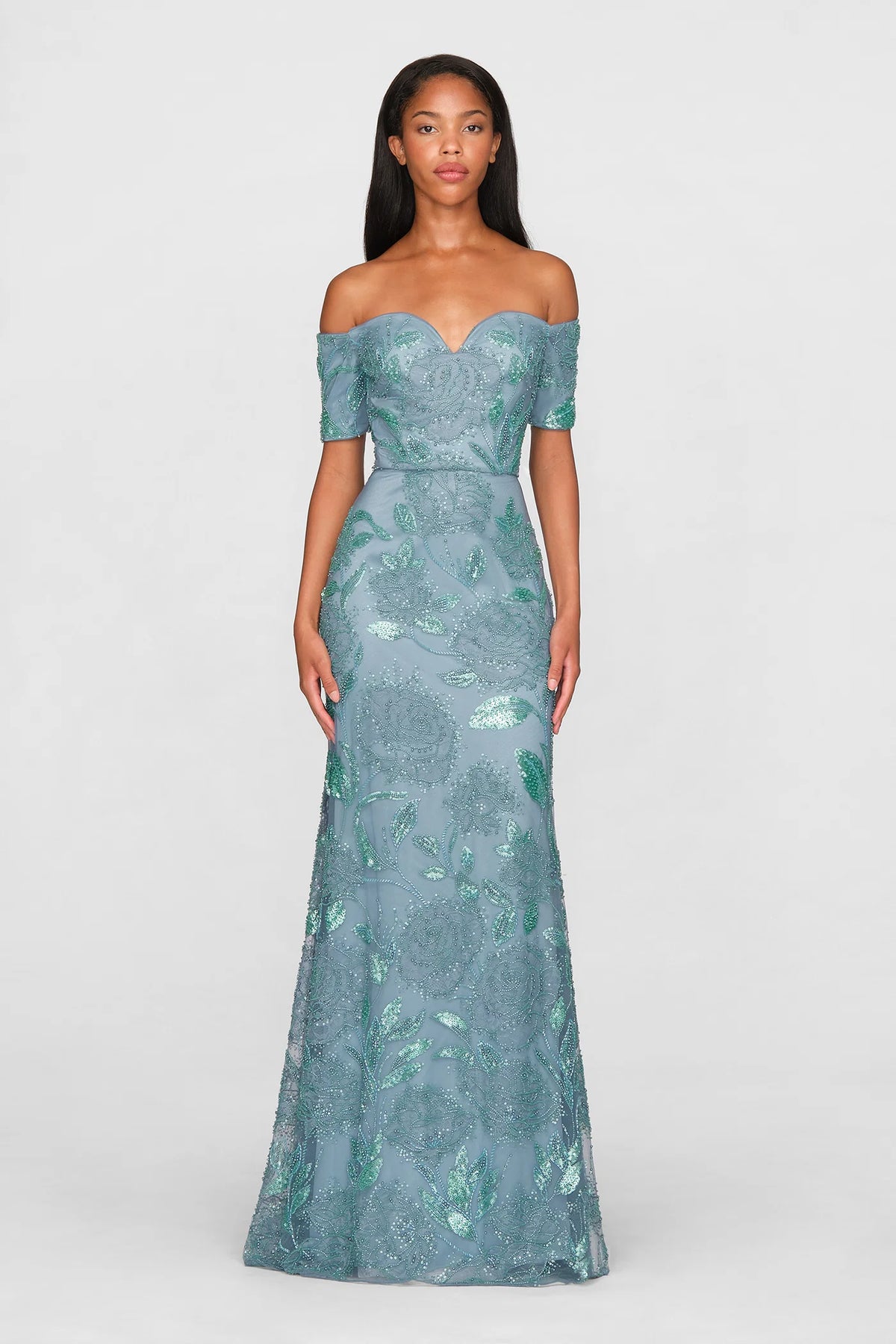 A model showcases a stunning teal blue gown with an off-the-shoulder neckline and intricate hand-beaded floral designs. Perfect for events like galas or weddings, this elegant dress is conveniently available near Apex, Cary, and Raleigh.