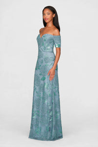 A model showcases a stunning teal blue off-shoulder gown adorned with intricate beading and floral patterns.