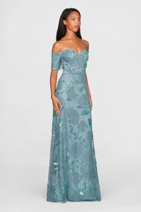 A model showcases a stunning teal blue gown adorned with intricate tonal rose beading and an elegant off-the-shoulder neckline.