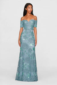 A model showcases a stunning teal blue off-shoulder gown adorned with intricate beading and tonal rose patterns.