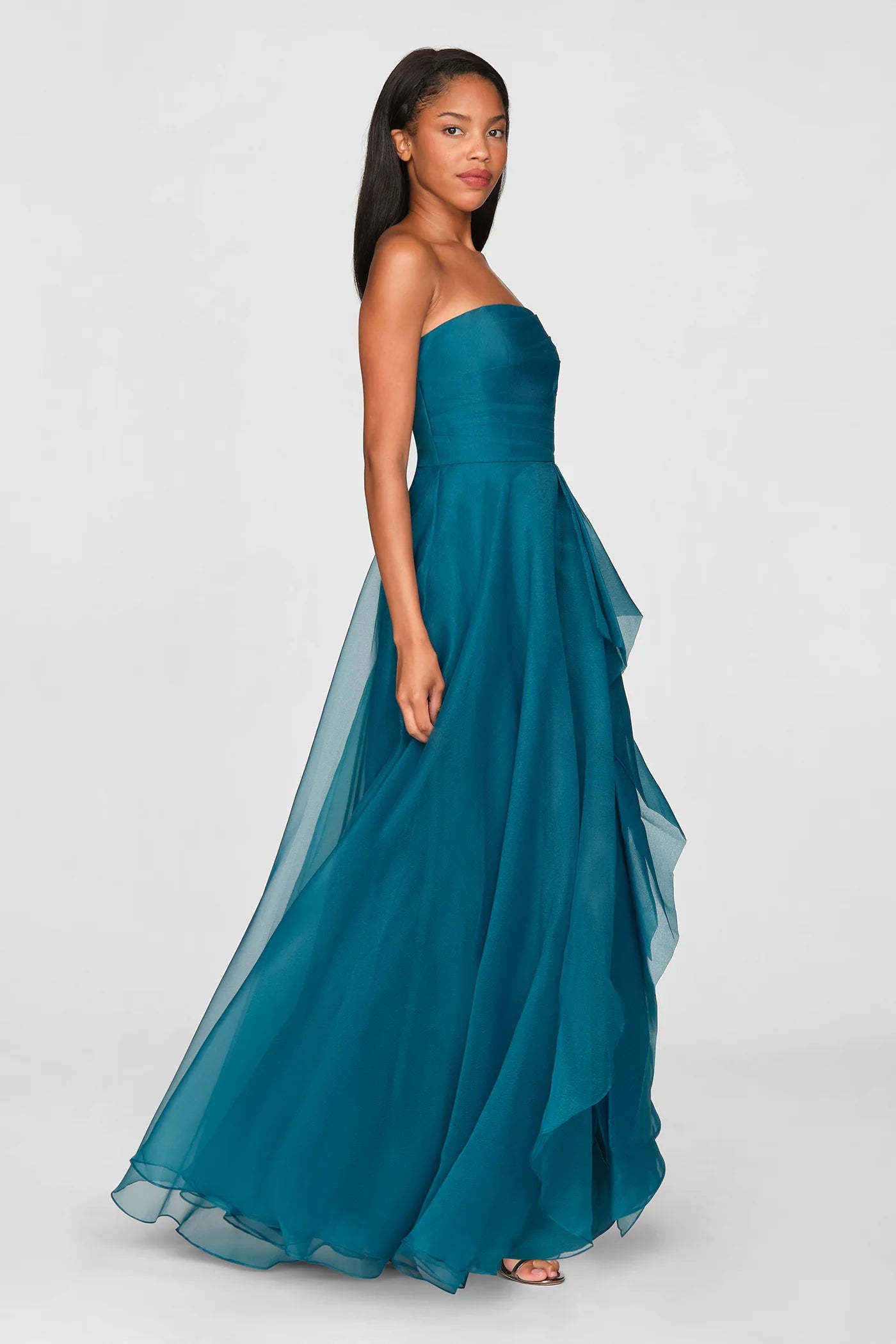A model poses in a stunning teal strapless gown with draped layers, perfect for formal occasions like prom, galas, or weddings. This elegant dress is conveniently available near Apex, Cary, and Raleigh.