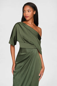 A model showcases a sleek, one-shoulder draped gown in a rich green satin fabric. This elegant dress is perfect for formal occasions such as black tie weddings or galas and is conveniently located near Apex, Cary, and Raleigh.