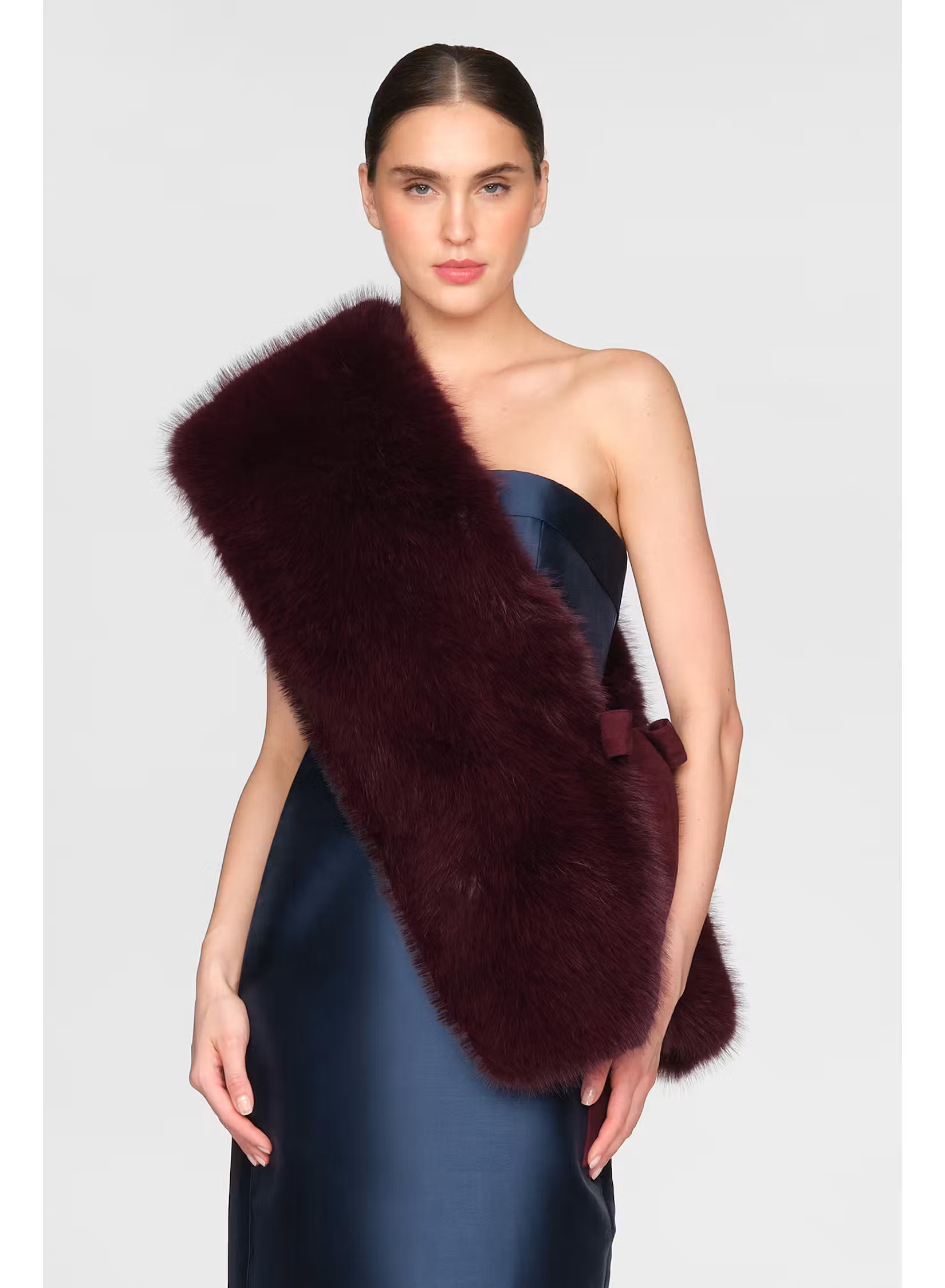 A model showcases a luxurious Kay Faux Fox Stole in Velvet Fig, draped elegantly over her shoulder. This stylish accessory adds warmth and sophistication to evening gowns, perfect for occasions like black tie weddings or galas.