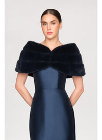 A model showcases a luxurious navy faux mink shawl draped elegantly over a sleek, fitted gown. This stylish accessory is perfect for formal occasions like black tie weddings or galas, and is conveniently available near Apex, Cary,.