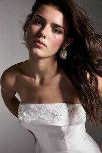 A model poses elegantly in a strapless white dress featuring intricate beading on the bodice. This sophisticated gown is ideal for special occasions like weddings or galas and is conveniently available near Apex, Cary, and Raleigh.