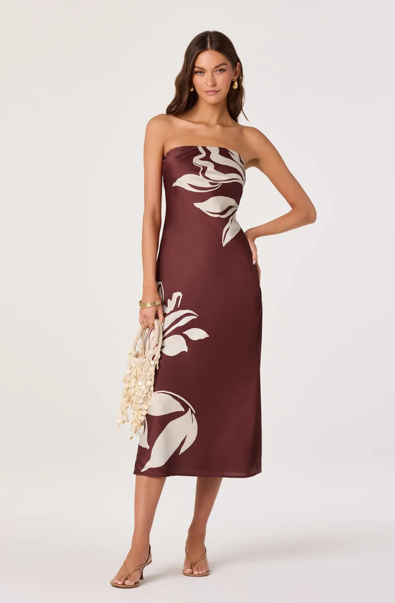 A model showcases a burgundy strapless maxi dress adorned with large floral designs in white. This elegant gown is perfect for formal occasions like weddings or galas and is conveniently located near Apex, Cary, and Raleigh.