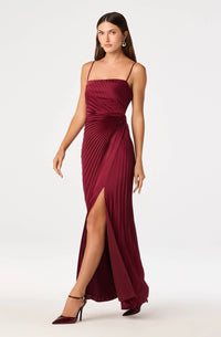 A model showcases a rich burgundy satin maxi dress featuring elegant sunburst pleating, adjustable spaghetti straps, and a leg slit.