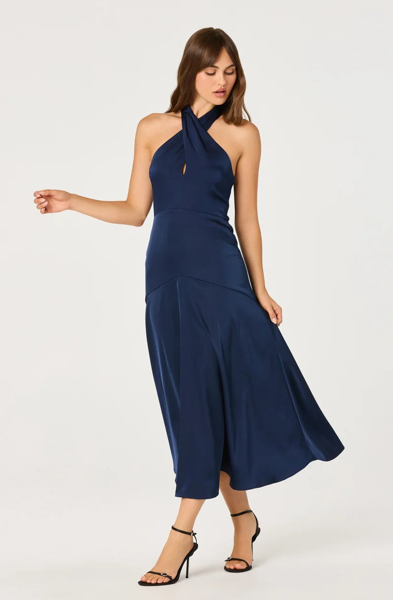 A model showcases a sleek navy satin dress featuring a halter neckline and a keyhole cutout. This elegant gown is perfect for special occasions like prom or galas, and is conveniently available near Apex, Cary, and Raleigh.