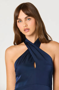 A model showcases a deep navy satin dress featuring a halter neck design with a keyhole cutout, perfect for formal occasions like weddings or galas. This elegant piece is conveniently available near Apex, Cary, and Raleigh.
