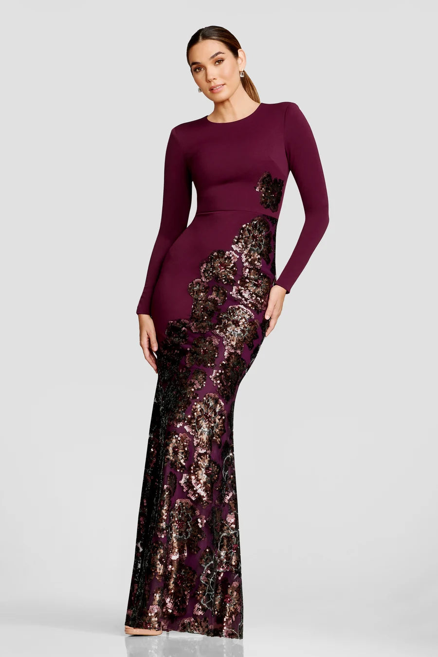A model showcases a stunning floor-length gown featuring a fitted burgundy bodice and a shimmering sequin-embellished skirt with floral designs.