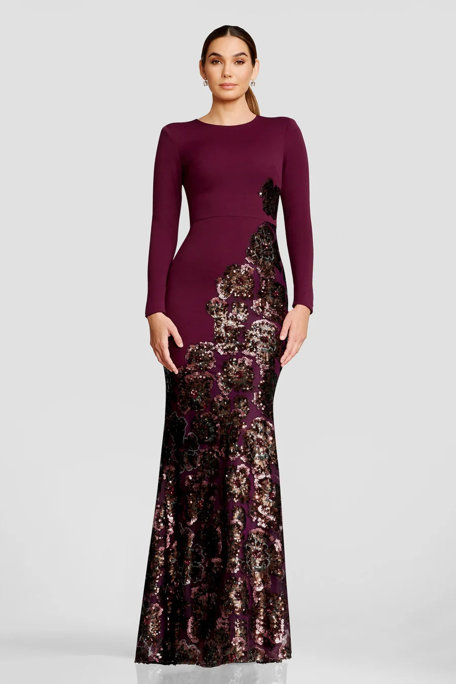 A model showcases a stunning long-sleeve gown in deep plum, featuring intricate floral sequin detailing along the hem.
