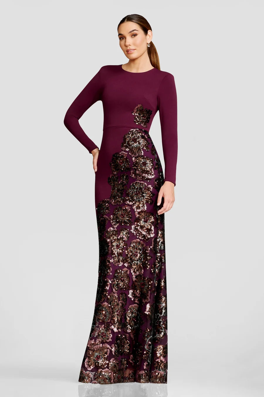 A model showcases a stunning floor-length gown featuring a rich burgundy color with intricate floral sequin detailing along the skirt.