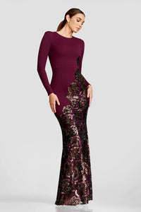 A model showcases a stunning floor-length gown in deep burgundy, featuring long sleeves and intricate floral sequin detailing at the hem. Perfect for a black tie wedding or gala, this elegant dress is available near Apex, Cary, and Raleigh.