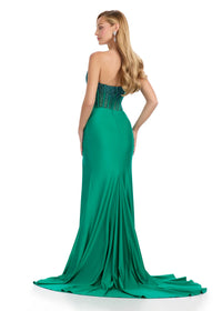 A model showcases a stunning emerald green strapless gown with a corset bustier and flowing skirt, perfect for occasions like prom, galas, or black tie weddings. This elegant dress is conveniently located near Apex, Cary, and Raleigh.