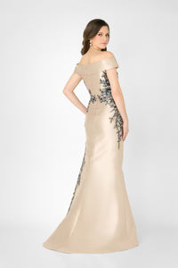 A woman is shown from the back in an off-the-shoulder champagne gown adorned with intricate black lace detailing.