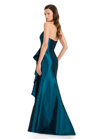 A woman in a dark teal strapless gown stands with her back to the camera, showcasing the dresss elegant silhouette and dramatic ruffle detail.