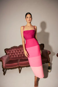 A model showcases a stylish square neck gown featuring a vibrant pink ombre design, standing confidently in front of a vintage pink sofa.