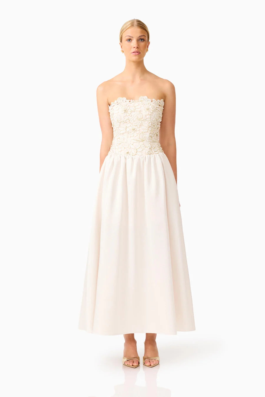 A model stands elegantly in a strapless ivory gown adorned with floral lace detailing at the bodice and a flowing skirt.