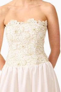 The image shows a close-up of a strapless gown featuring intricate floral embroidery and beadwork on the bodice, transitioning to a flowing white skirt.
