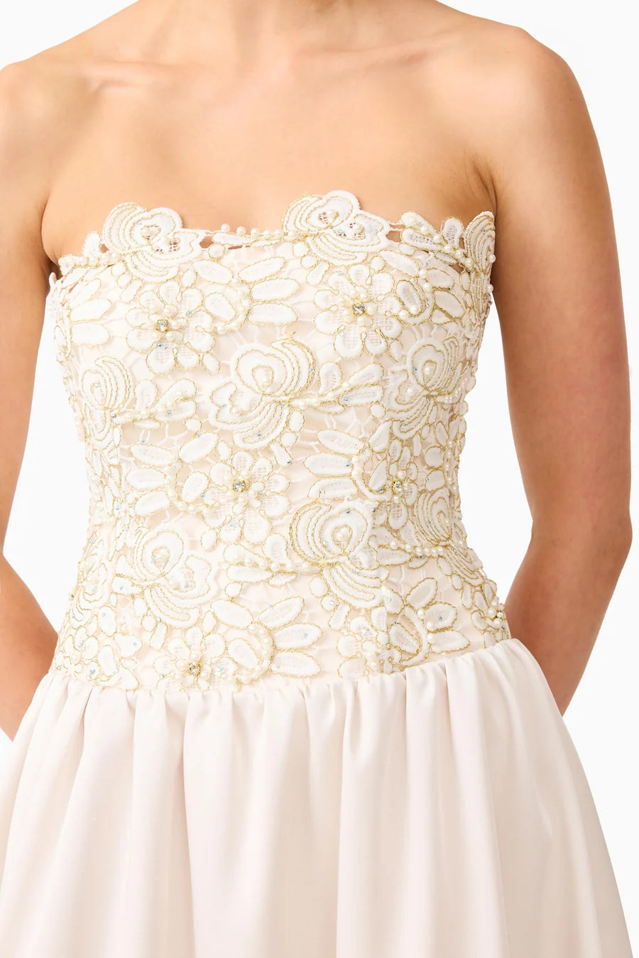 The image shows a close-up of a strapless gown featuring intricate floral embroidery and beadwork on the bodice, transitioning to a flowing white skirt.