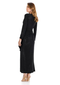 A woman is wearing a full-length black gown with long sleeves and a ruched design, elegantly showcasing a shimmering fabric.