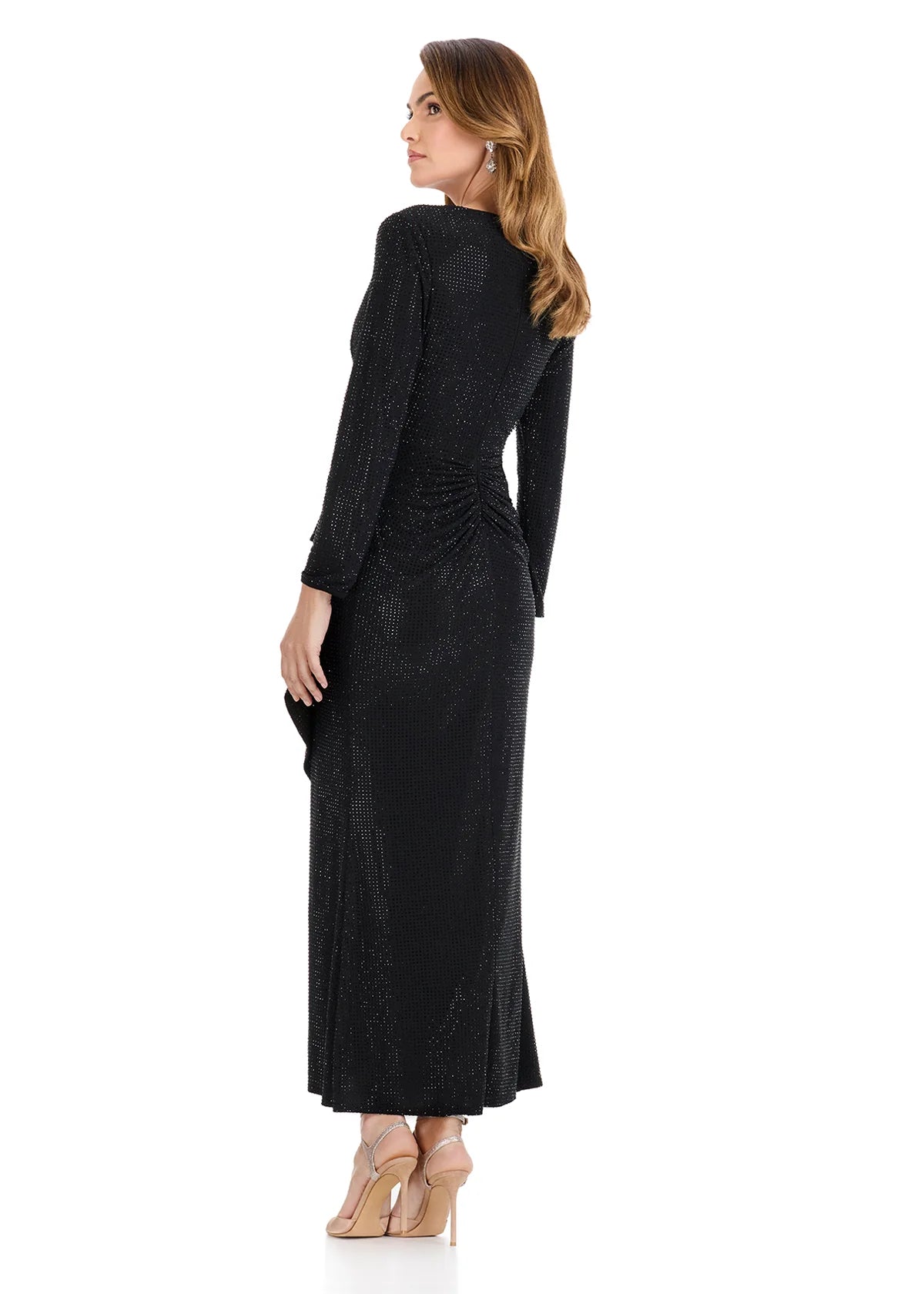 A woman is wearing a full-length black gown with long sleeves and a ruched design, elegantly showcasing a shimmering fabric.