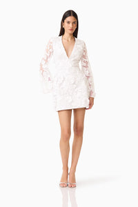 A model showcases the Lorina Flared Sleeve Mini Dress in White, featuring a flattering V-neckline and elegant 3D floral design. Perfect for occasions like prom or a gala, this dress is conveniently available near Apex, Cary, and Raleigh.