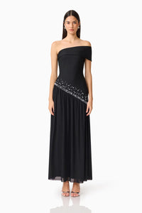 A model showcases the elegant Natasia Off-Shoulder Gown in black, featuring a fitted bodice and a flowing skirt adorned with subtle embellishments.
