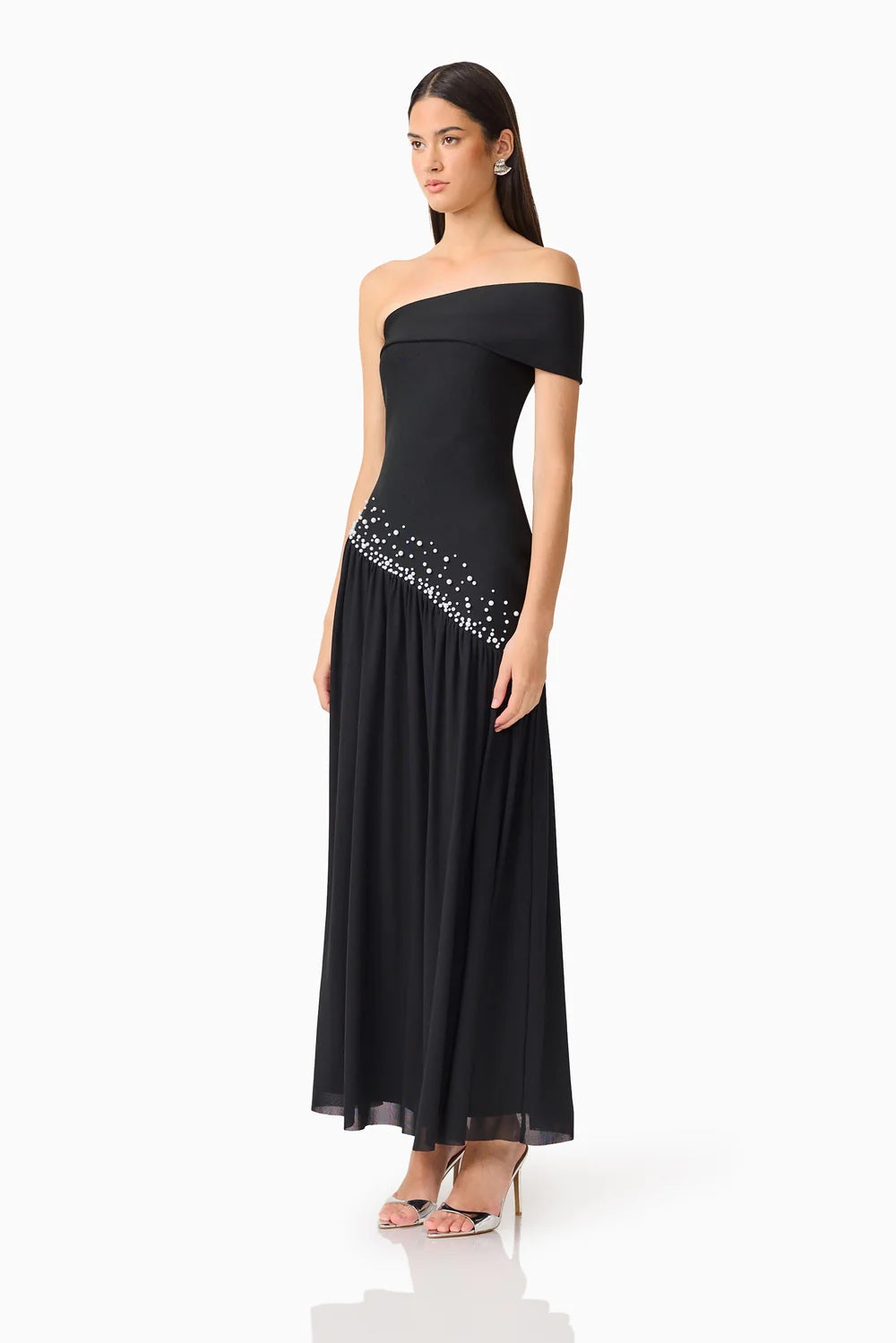 A model showcases a stunning black off-shoulder gown, featuring a fitted bodice and a flowing skirt adorned with delicate embellishments.