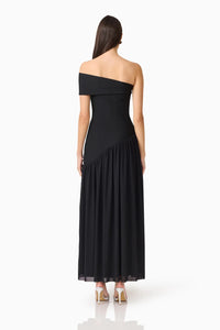 A woman stands in profile wearing a sleek, off-shoulder black gown with a flowing skirt, showcasing a refined evening silhouette.