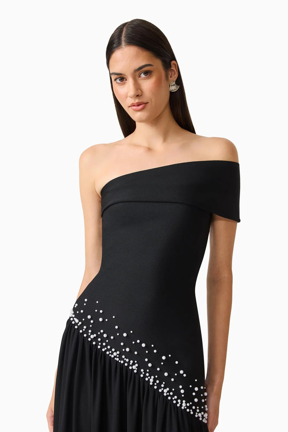 A model poses in an elegant off-shoulder black gown featuring a sparkling bead design along the hem. This stunning dress is perfect for formal events like galas or black tie weddings, conveniently located near Apex, Cary, and Raleigh.