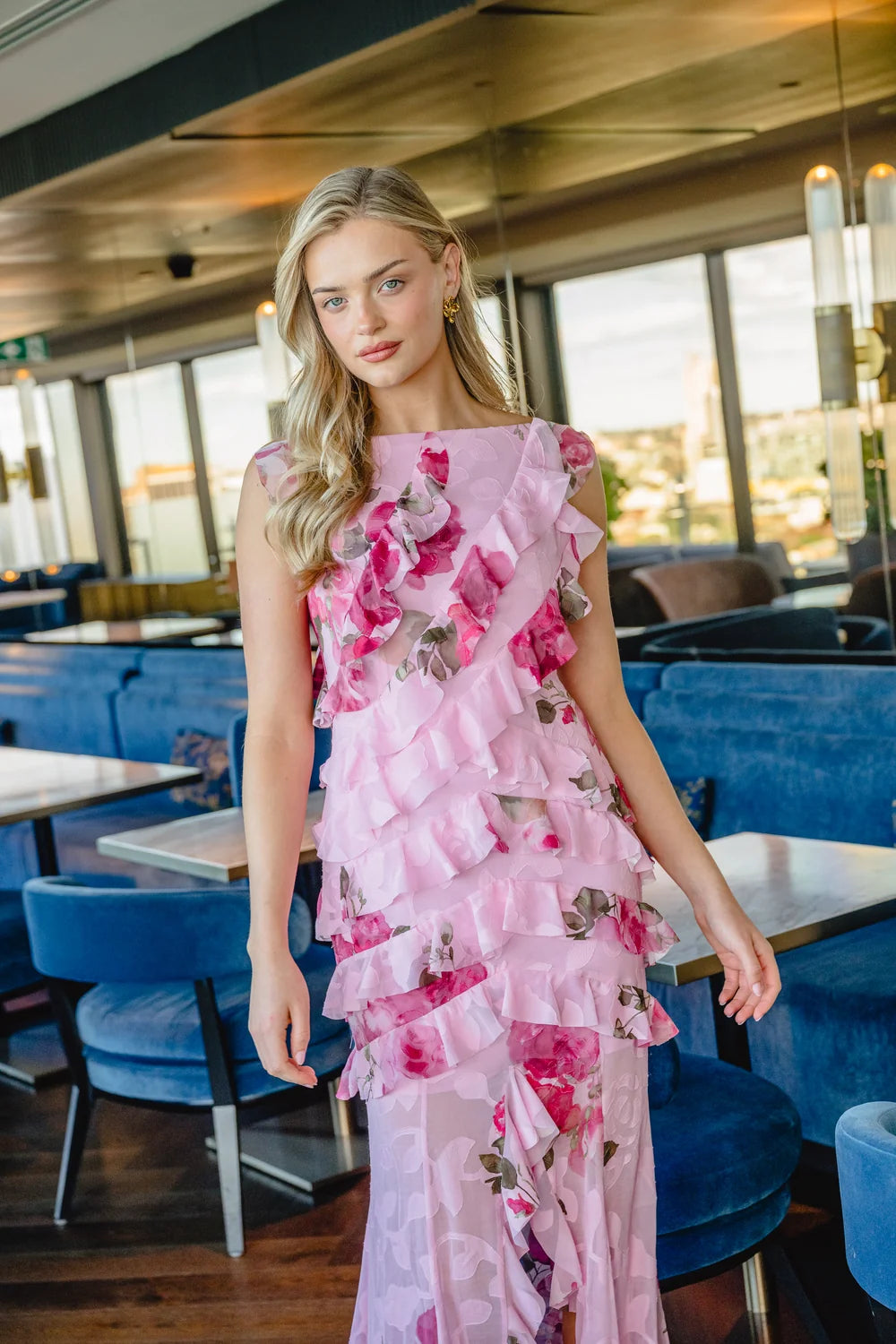 A model poses in a stunning pink floral gown with ruffled details, perfect for elegant occasions like mother of the bride or gala events.
