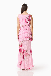 A woman is seen from the back wearing a sleeveless pink floral gown featuring ruffled layers, ideal for elegant occasions such as weddings, proms, or galas. This stunning dress is conveniently available near Apex, Cary, and Raleigh.