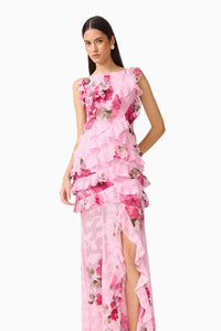 A model wears a stunning pink floral gown featuring layers of ruffles and a thigh-high slit, perfect for elegant occasions such as weddings, proms, or galas. This dress is conveniently located near Apex, Cary, and Raleigh.