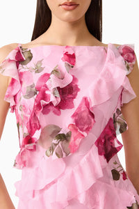 A close-up view of a woman wearing a pink floral gown featuring ruffled detailing across the bodice. This elegant dress is perfect for special occasions like weddings or galas, and is located conveniently near Apex, Cary, and Raleigh.