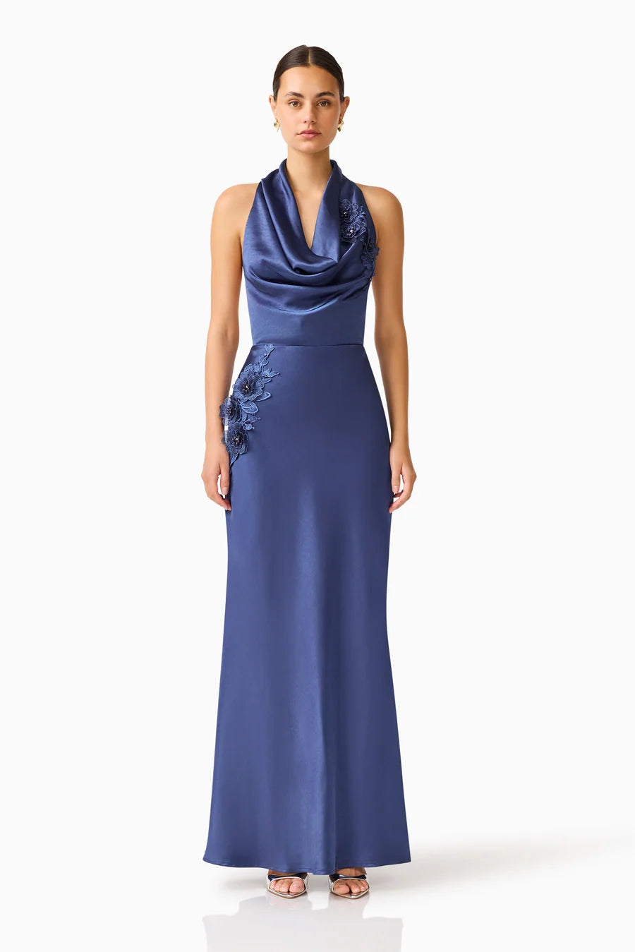 A woman stands in a stunning navy cowl neck gown featuring elegant floral embroidery on one side, perfect for formal events like galas, black tie weddings, or mother of the bride occasions.