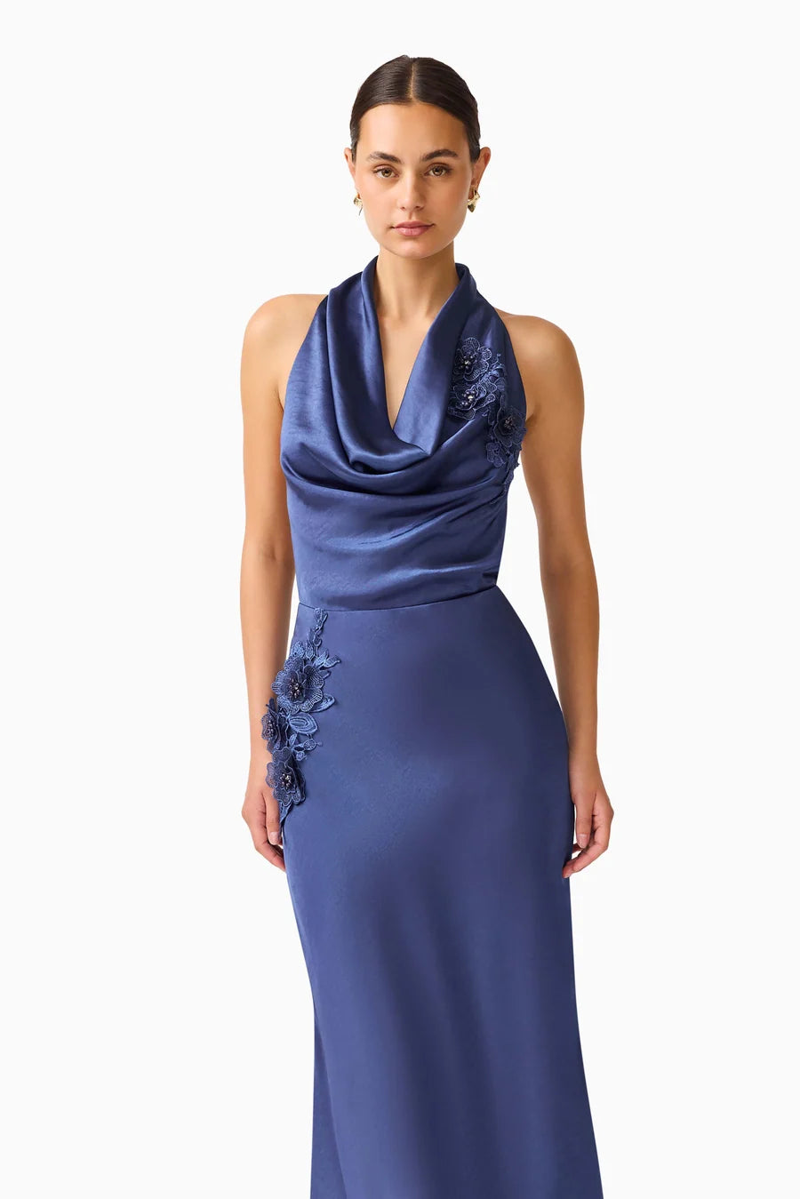 A model showcases a sophisticated navy cowl neck gown featuring elegant floral embroidery on one side. This stunning dress is perfect for memorable occasions like galas or black tie weddings, and is available near Apex, Cary, and Raleigh.