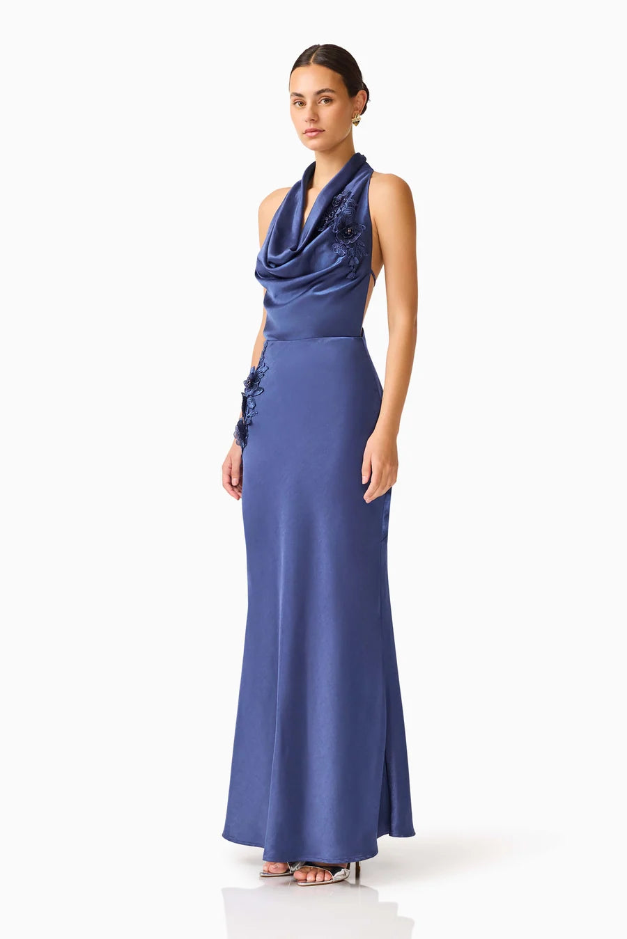 A model poses elegantly in a navy cowl neck gown featuring floral embellishments. This sophisticated dress is perfect for memorable occasions such as a gala or black tie wedding, conveniently located near Apex, Cary, and Raleigh.