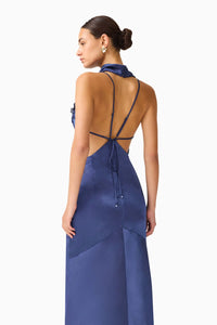 Elegant woman wearing a navy cowl neck gown with an open back and delicate straps, showcasing a fluid silhouette.