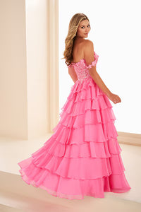 A model showcases a stunning hot pink gown with a layered ruffle design and off-the-shoulder lace straps.