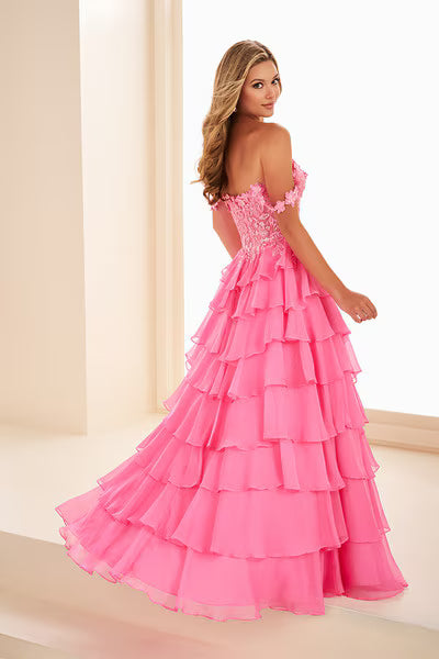 A model showcases a stunning hot pink gown with a layered ruffle design and off-the-shoulder lace straps.