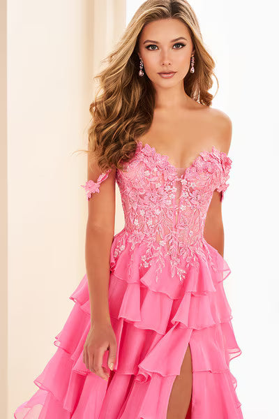 A model poses in a stunning hot pink gown featuring off-the-shoulder straps and three-dimensional floral lace detailing. This elegant dress, perfect for prom or a gala, is available near Apex, Cary, and Raleigh.