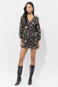 A model poses in a floral-patterned mini dress with a deep V-neckline and long, puffed sleeves. This stylish outfit is perfect for casual outings like birthday parties or date nights and is conveniently available near Apex, Cary,.
